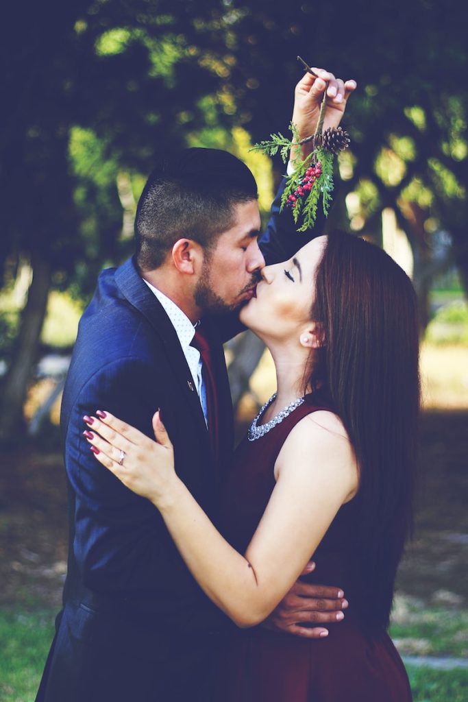 man and woman kissing near trees ex back